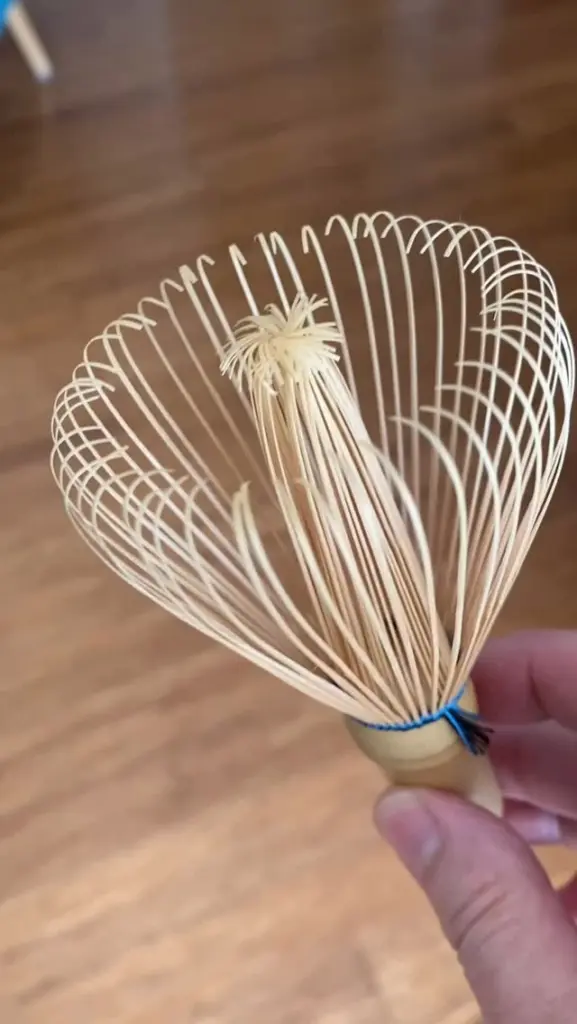 Hand holding a bamboo tea whisk with fine curved tines
