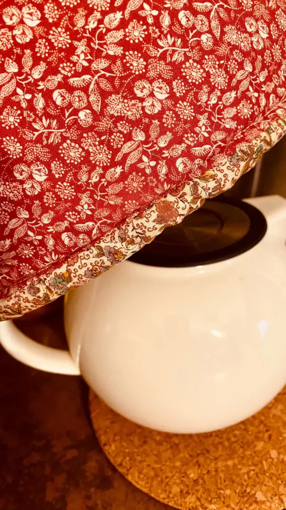 White ceramic teapot partially covered by red floral fabric