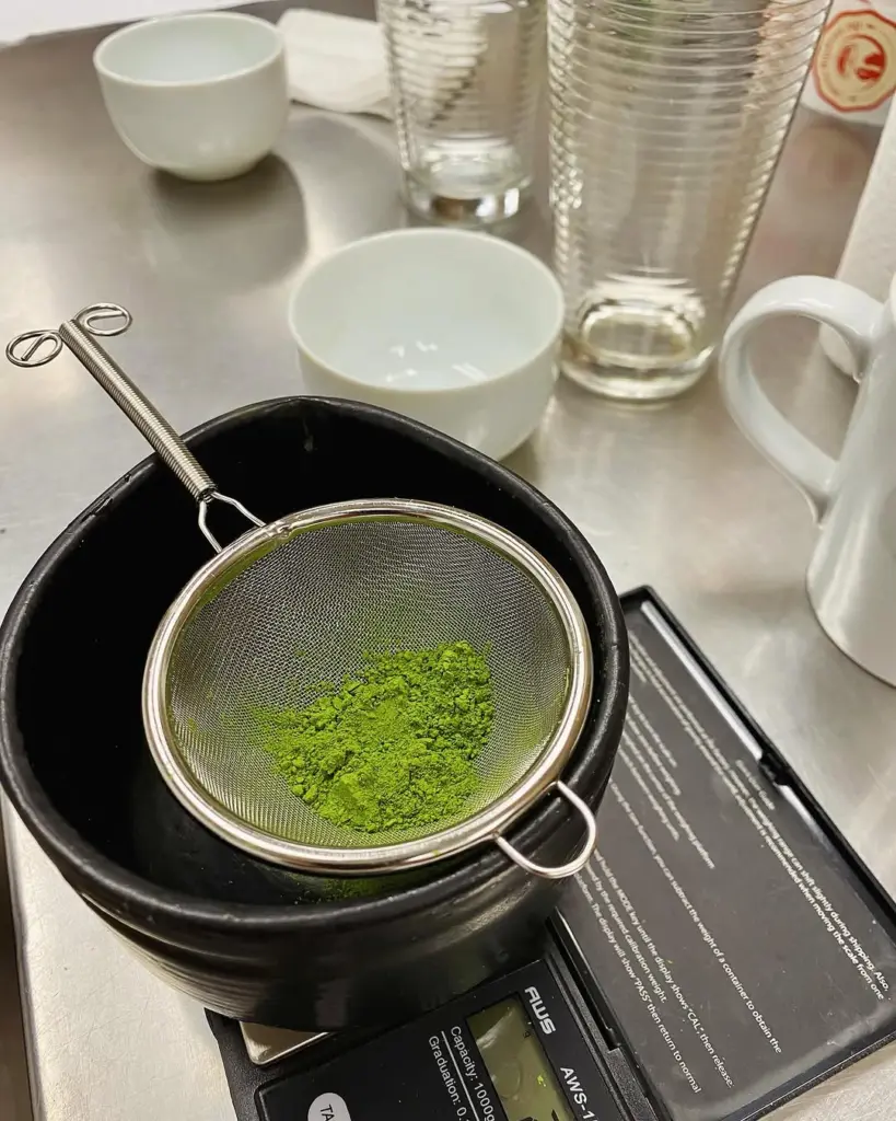 Bright green tea powder in a fine-mesh sieve over a black bowl
