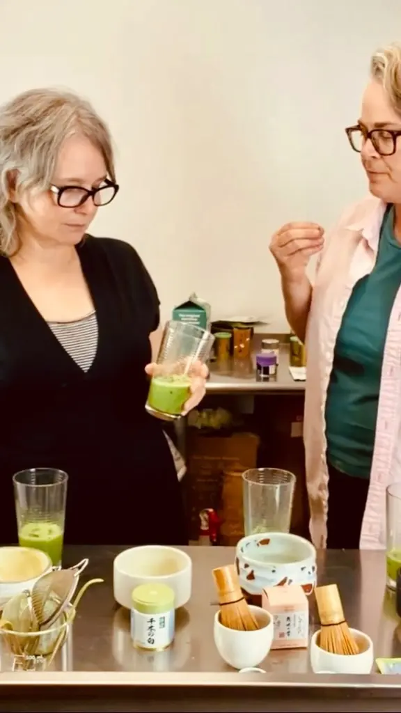 Two people tasting bright green matcha beside bowls, whisks, and cups