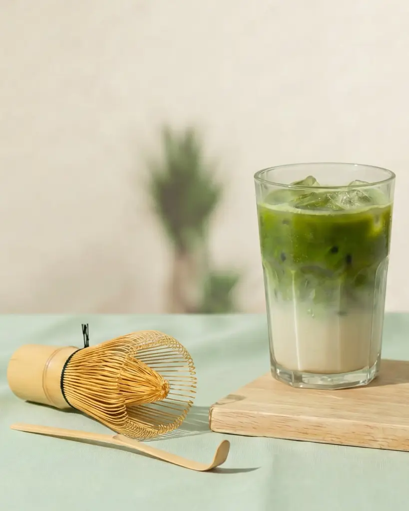 Layered iced matcha latte beside a bamboo whisk and scoop