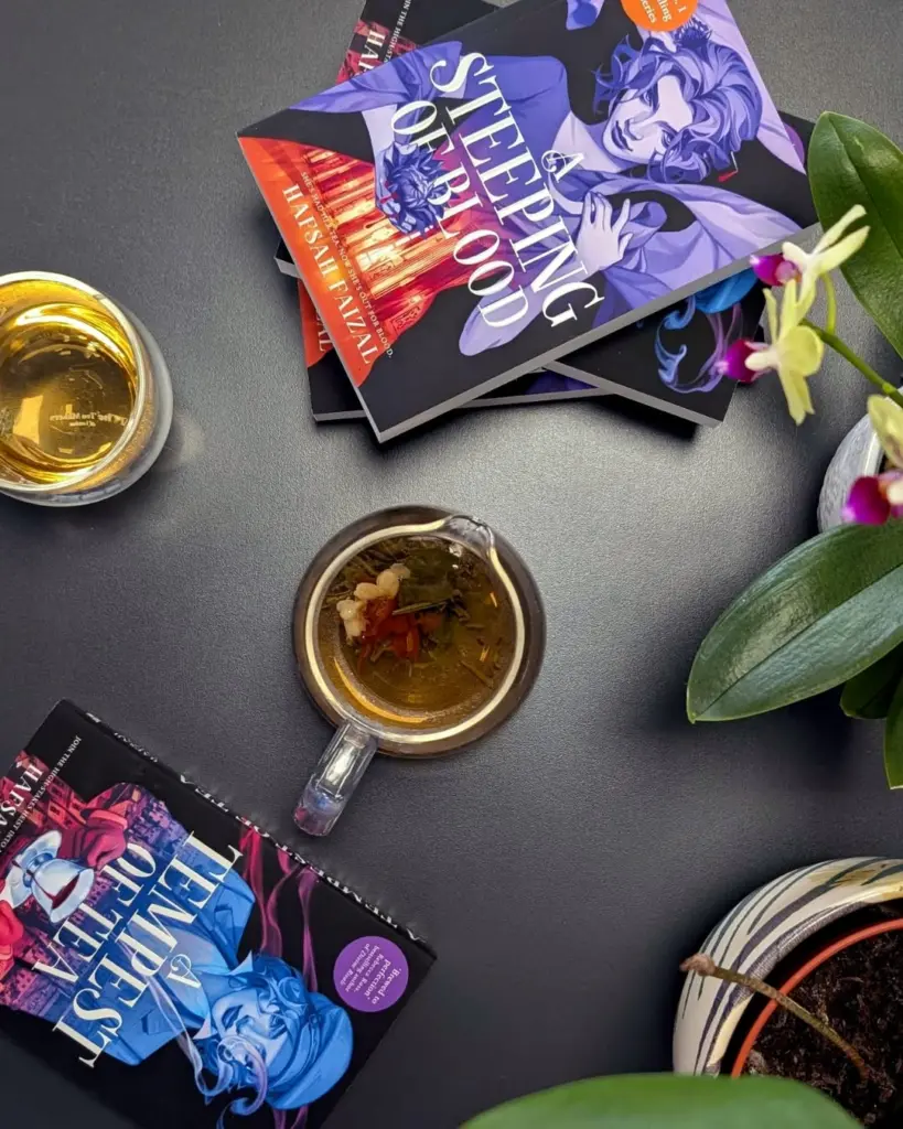 Glass cup of loose-leaf tea surrounded by colorful books and houseplants