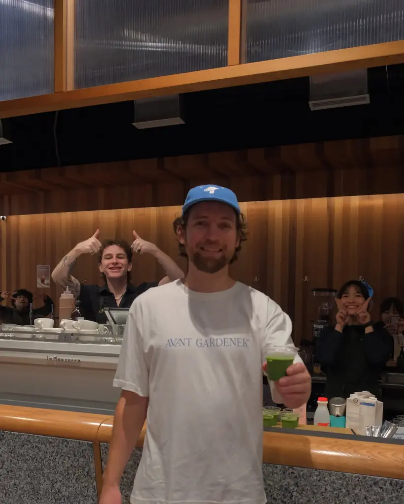 Smiling man holding a small cup of bright green matcha at a counter