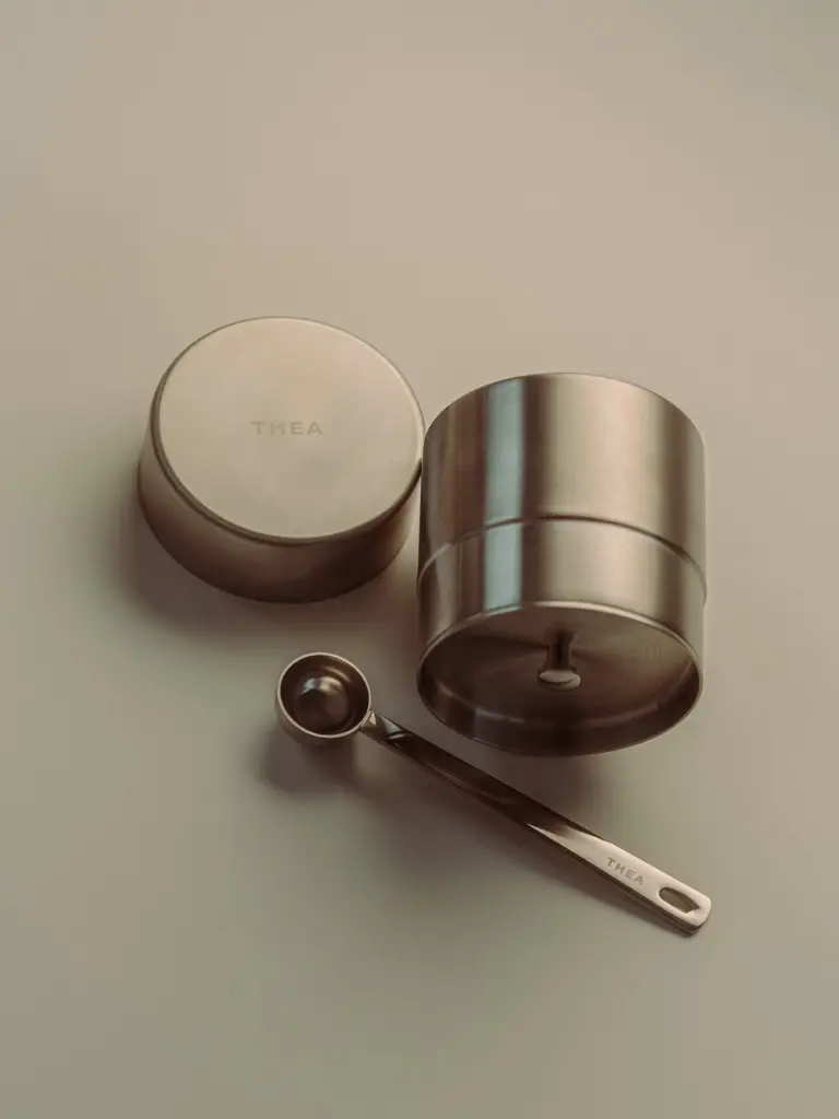 Metal sifter, lid, and measuring spoon on a neutral surface