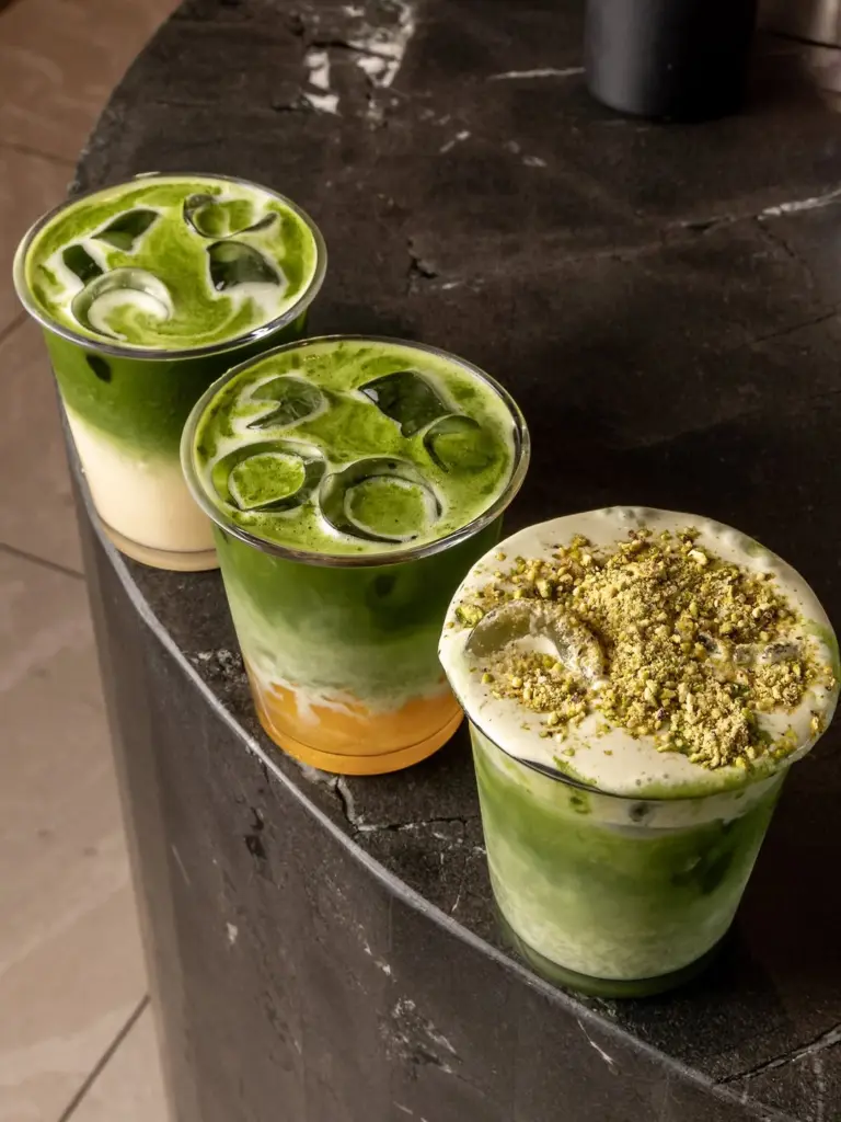 Three layered iced matcha drinks, one topped with crushed nuts