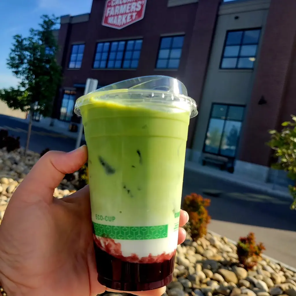 Hand holding a layered iced green drink outside Calgary Farmers’ Market