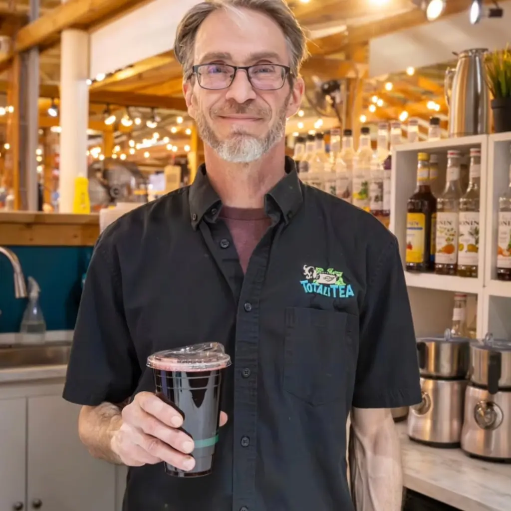 Smiling staff member in a TotaliTea shirt holding a dark cold drink