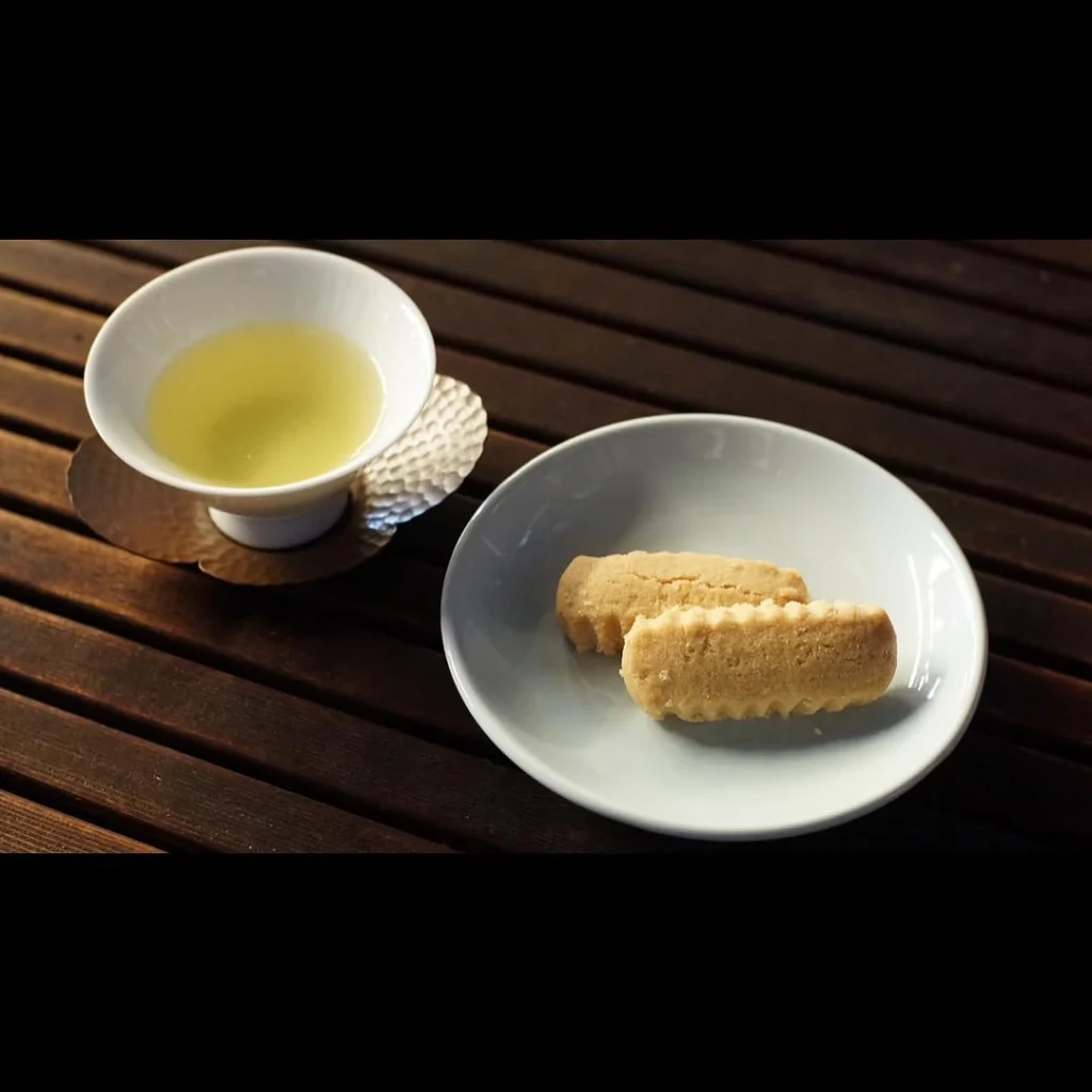 Cup of pale green tea beside two golden baked sweets