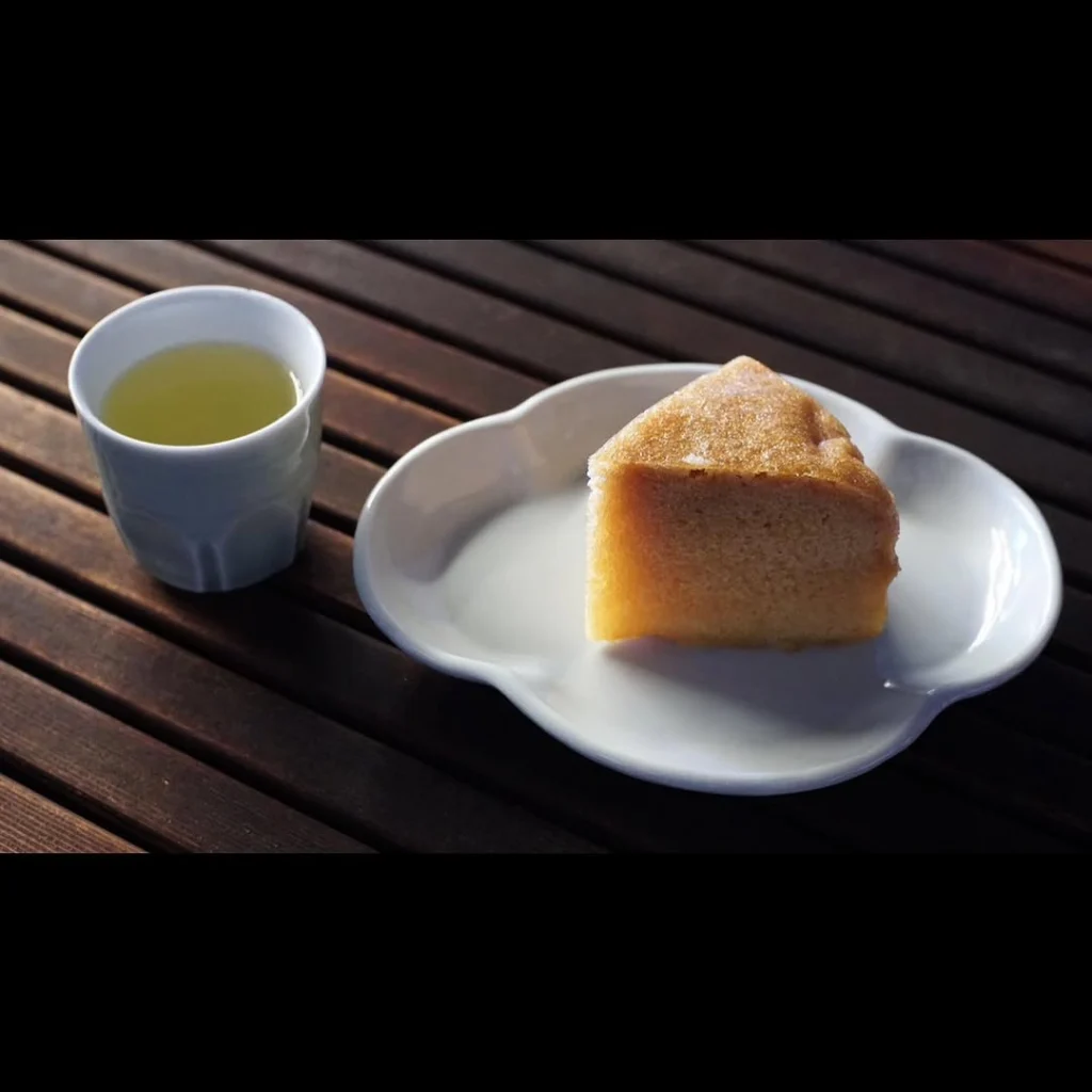 Cup of pale green tea beside a slice of golden cake