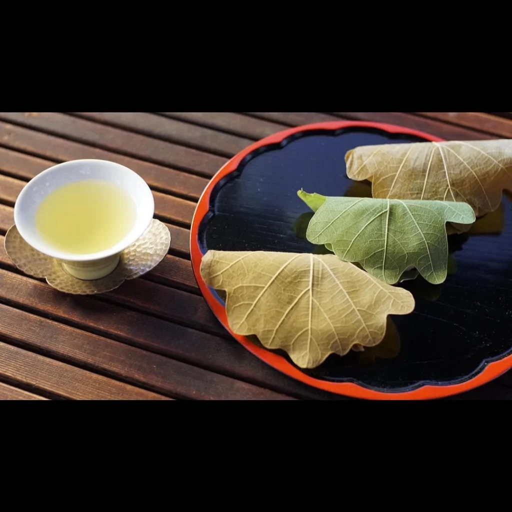 Cup of pale green tea beside three leaf-wrapped sweets