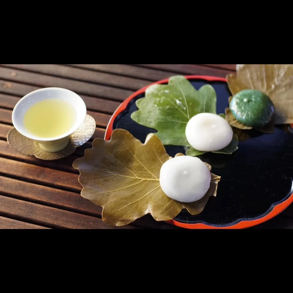 Pale green tea beside three round sweets arranged on leaves