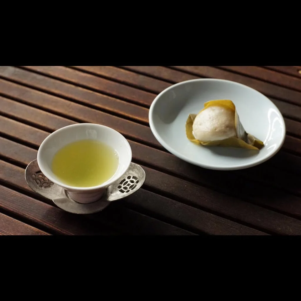 Cup of pale green tea beside a leaf-wrapped white sweet