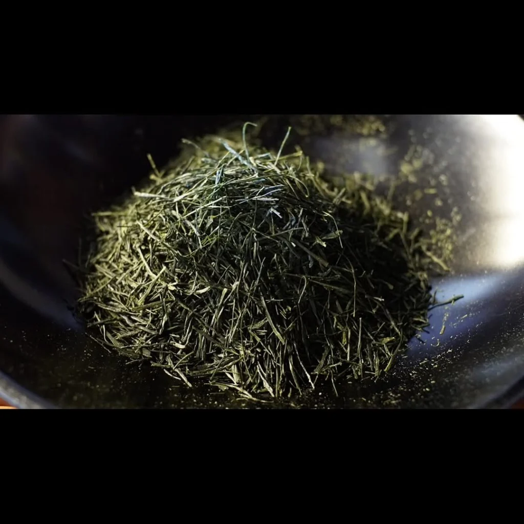 Close-up of loose green tea leaves in a dark bowl