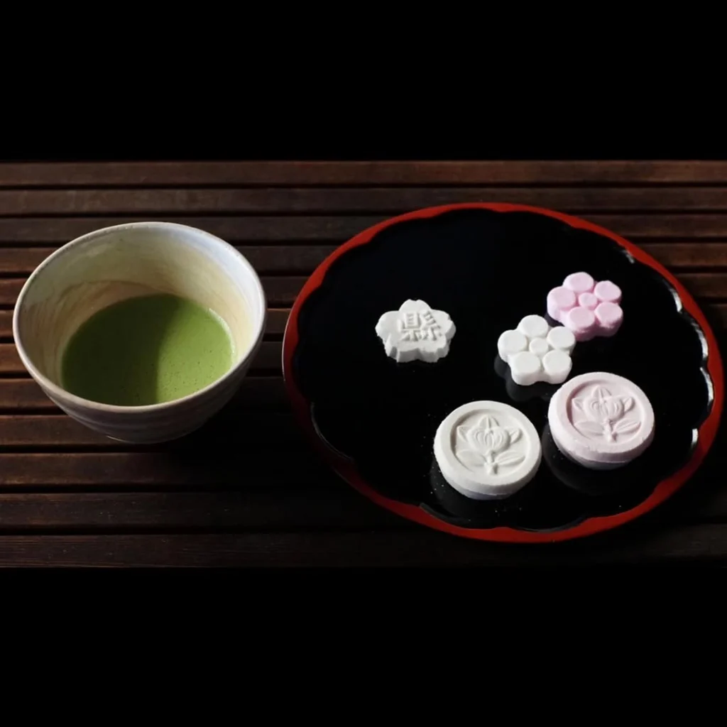 Bowl of green matcha beside white and pink molded sweets
