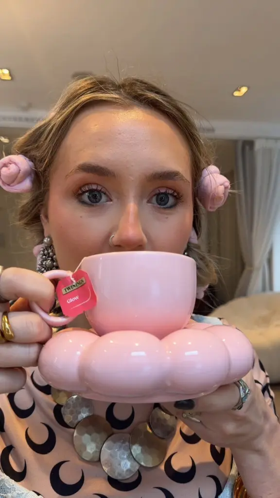 Woman holding a pink teacup and saucer with a Twinings Glow tea tag