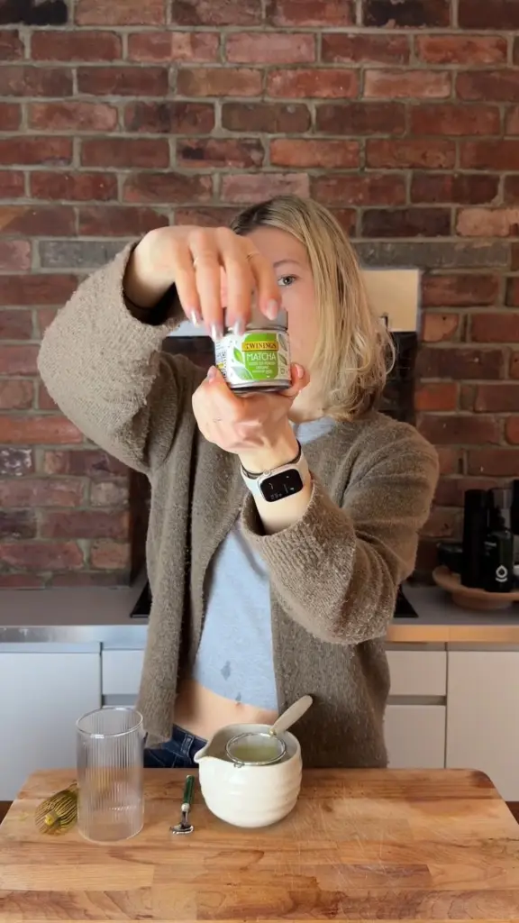 Person holding a Twinings matcha tin above tea-making utensils