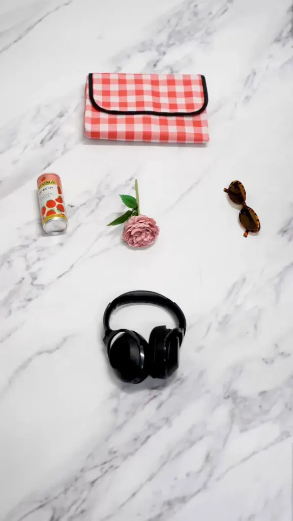 Twinings Refresh can, pink flower, sunglasses, headphones, and checkered pouch on marble