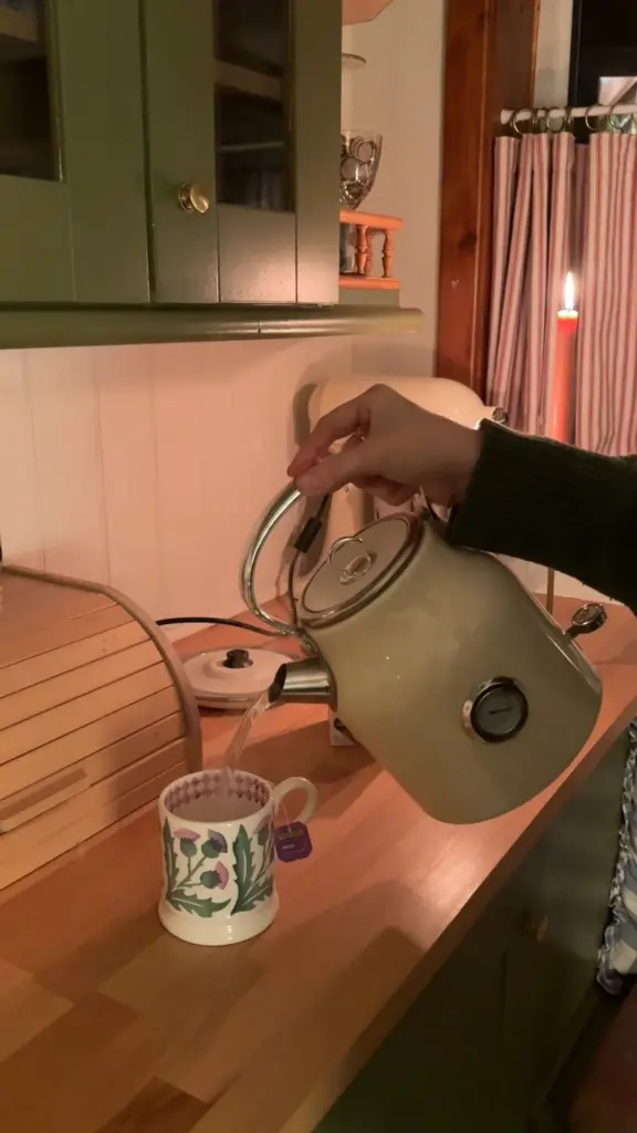 Hot water poured from a cream kettle into a floral mug with a Twinings tea bag