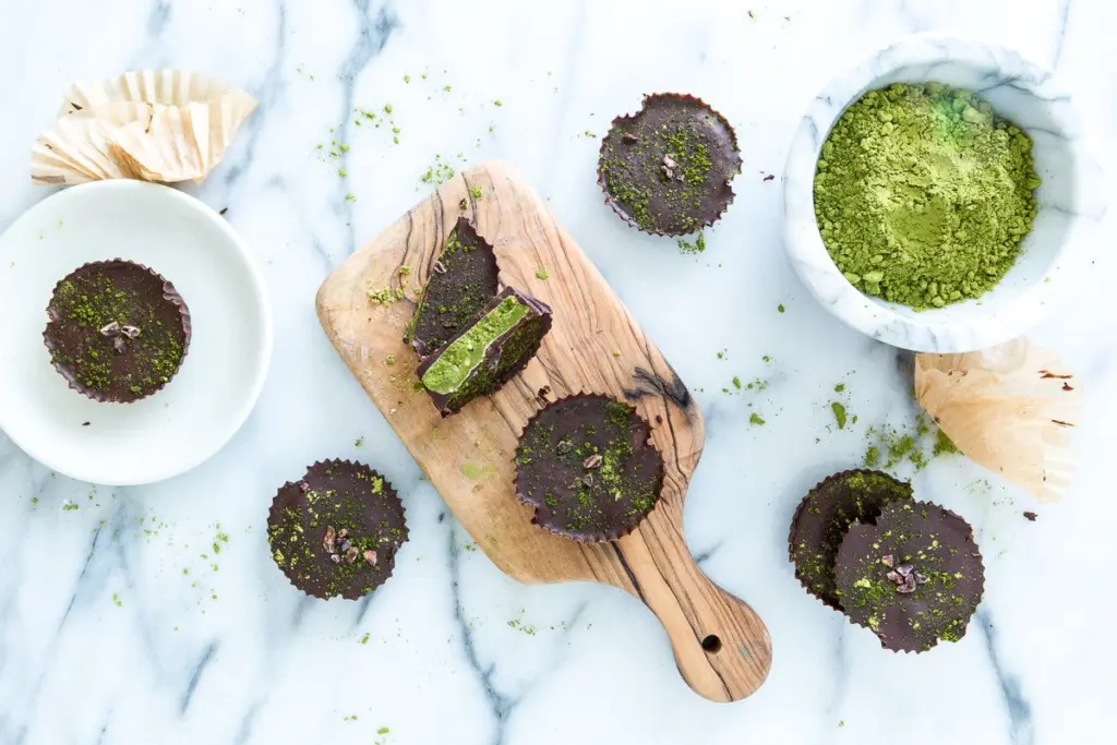 Chocolate cups dusted with green powder beside a bowl of green tea powder