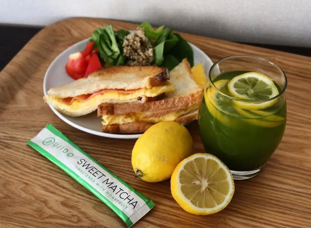 Green lemon drink beside sandwiches, salad, lemons, and an Ujido Sweet Matcha packet