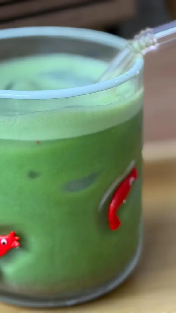 Frothy green drink in a decorated glass with a clear straw