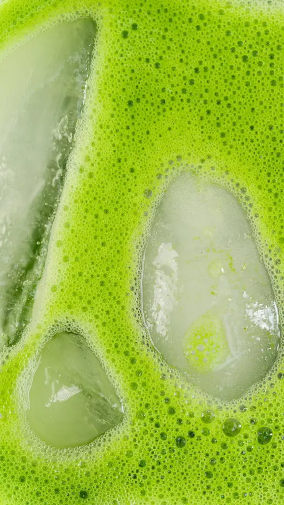 Bright green foamy drink surrounding large ice cubes