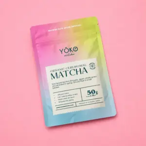 Angled Yōko Matcha Organic Ceremonial Matcha 50 g resealable pouch with a pink, yellow, and blue gradient on a pink background