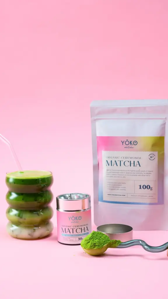 Matcha tins, pouch, powder-filled spoon, and layered iced green drink on a pink set
