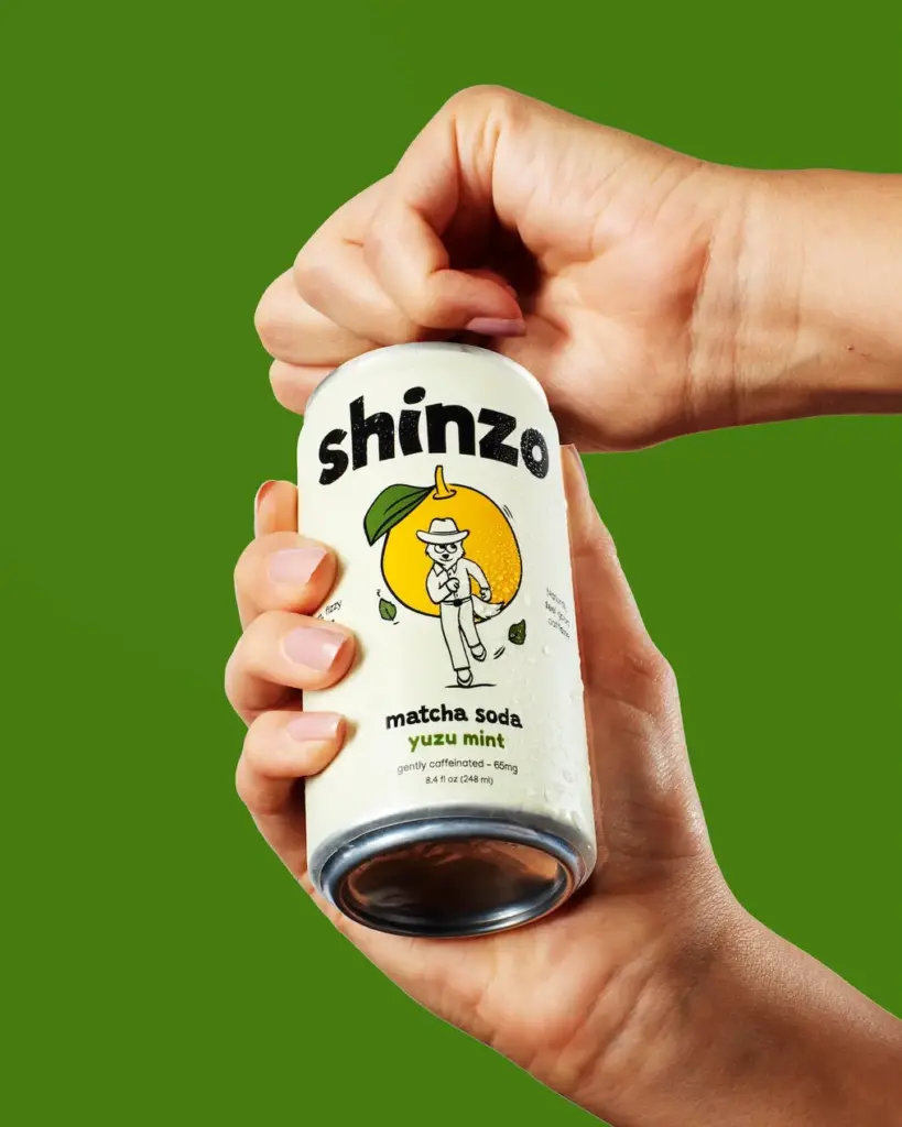 Two hands opening a can of Shinzo yuzu mint matcha soda against a green background