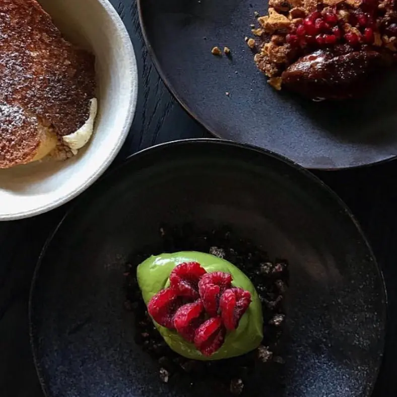 Green cream dessert topped with raspberries in a black bowl