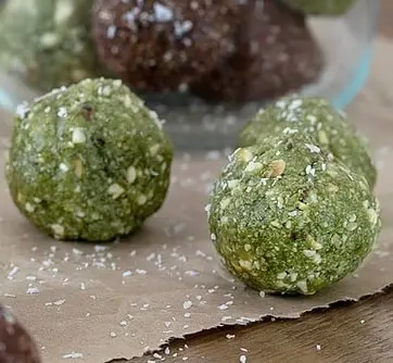 Two green snack balls with visible seeds and coconut flakes on brown paper