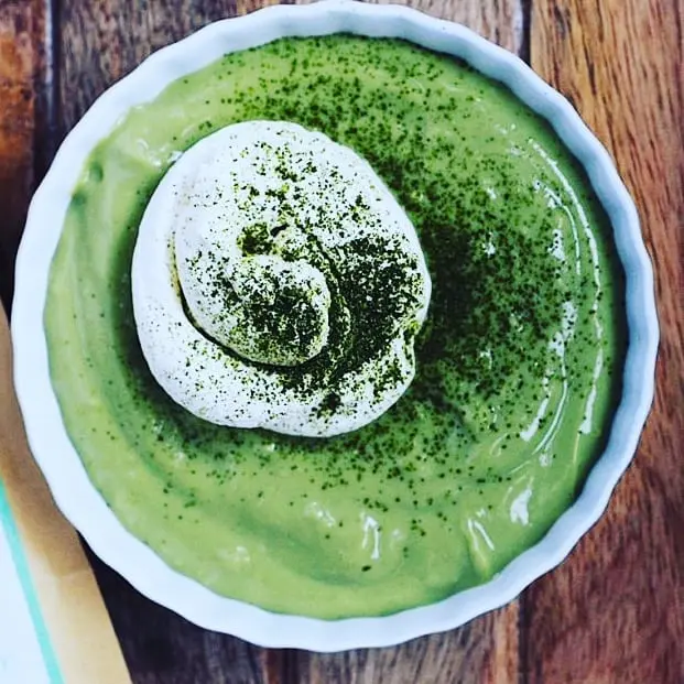 Bowl of creamy green dessert topped with white cream and dusted green powder