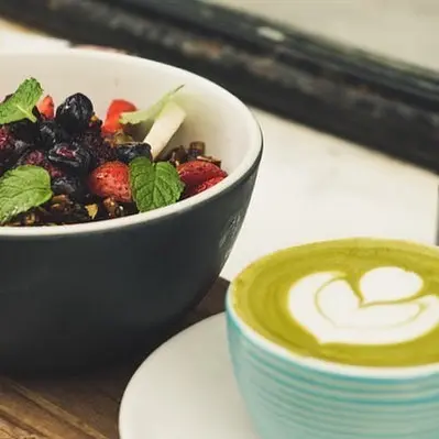 Small matcha latte with heart foam art beside a bowl of berries and mint