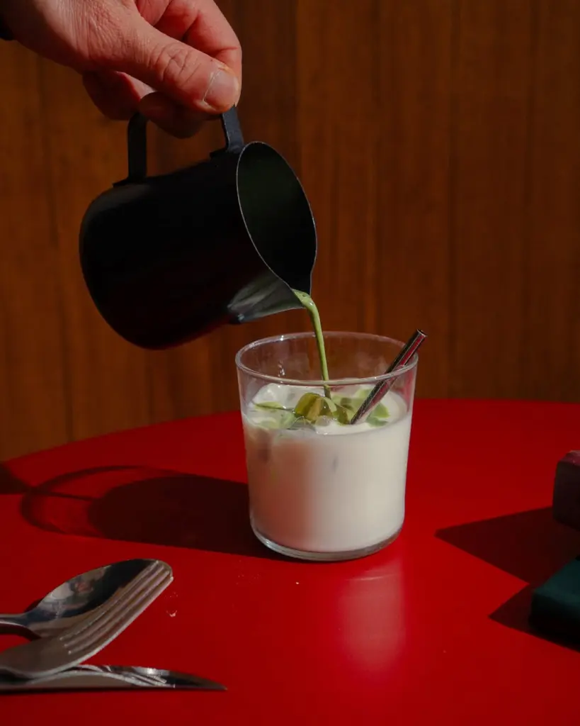 Green matcha being poured from a black pitcher into a glass of iced white liquid