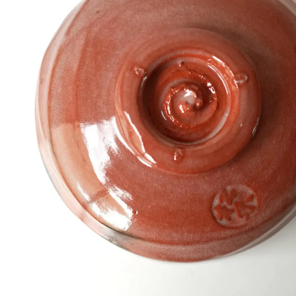 Underside of a glossy red ceramic bowl with a circular foot and stamped mark